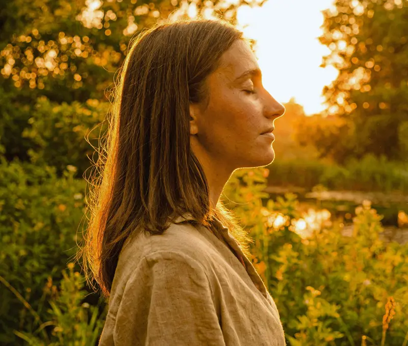 Mujer con los ojos cerrados a la luz del atardecer, conectando con su mundo interior
